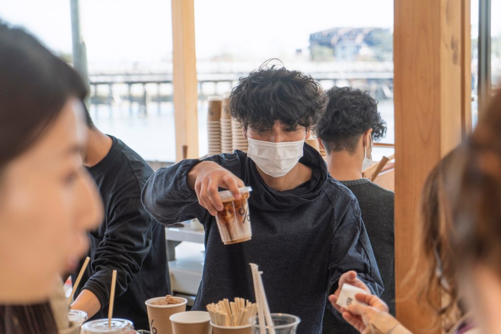 Coffee being served by man wearing a face mask. 